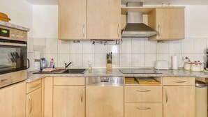 A modern kitchen with light wood cabinets, a stainless steel sink, and a built-in oven.