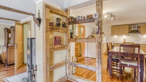 A rustic interior with exposed wooden beams, a dining area with wooden chairs, and a kitchen with wooden cabinets.