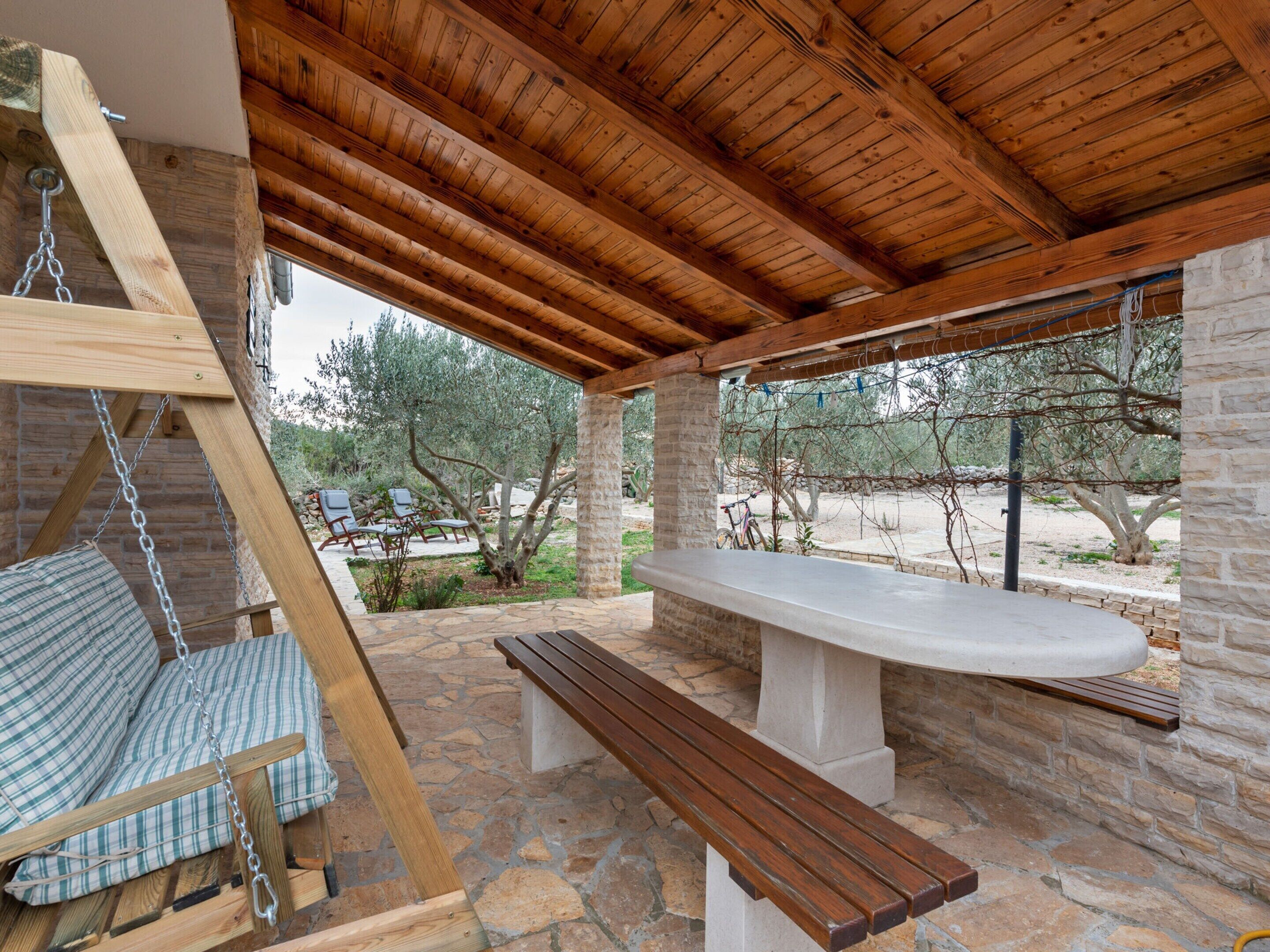 A covered outdoor seating area with a swing, a bench, and a table.