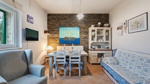 Un soggiorno con tavolo da pranzo, sedie, divano, televisore, quadro e credenza.