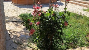 Un patio in pietra con vasca idromassaggio in legno, circondato da vegetazione lussureggiante e piante fiorite.