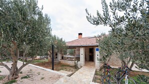Un vialetto in pietra conduce a un edificio con tetto in tegole, circondato da alberi di ulivo.