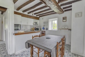 A kitchen with a dining table, wooden chairs, a window, and a clock on the wall. - Cozy Normandy Escape (Formigny La Bataille)