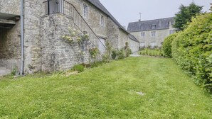 A stone building with a staircase leading to a balcony, a well-maintained lawn, and a hedge. - Cozy Normandy Escape (Formigny La Bataille)