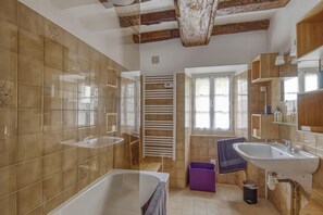 A bathroom with two sinks, a bathtub, wooden beams, a window, and a towel rack. - Cozy Normandy Escape (Formigny La Bataille)
