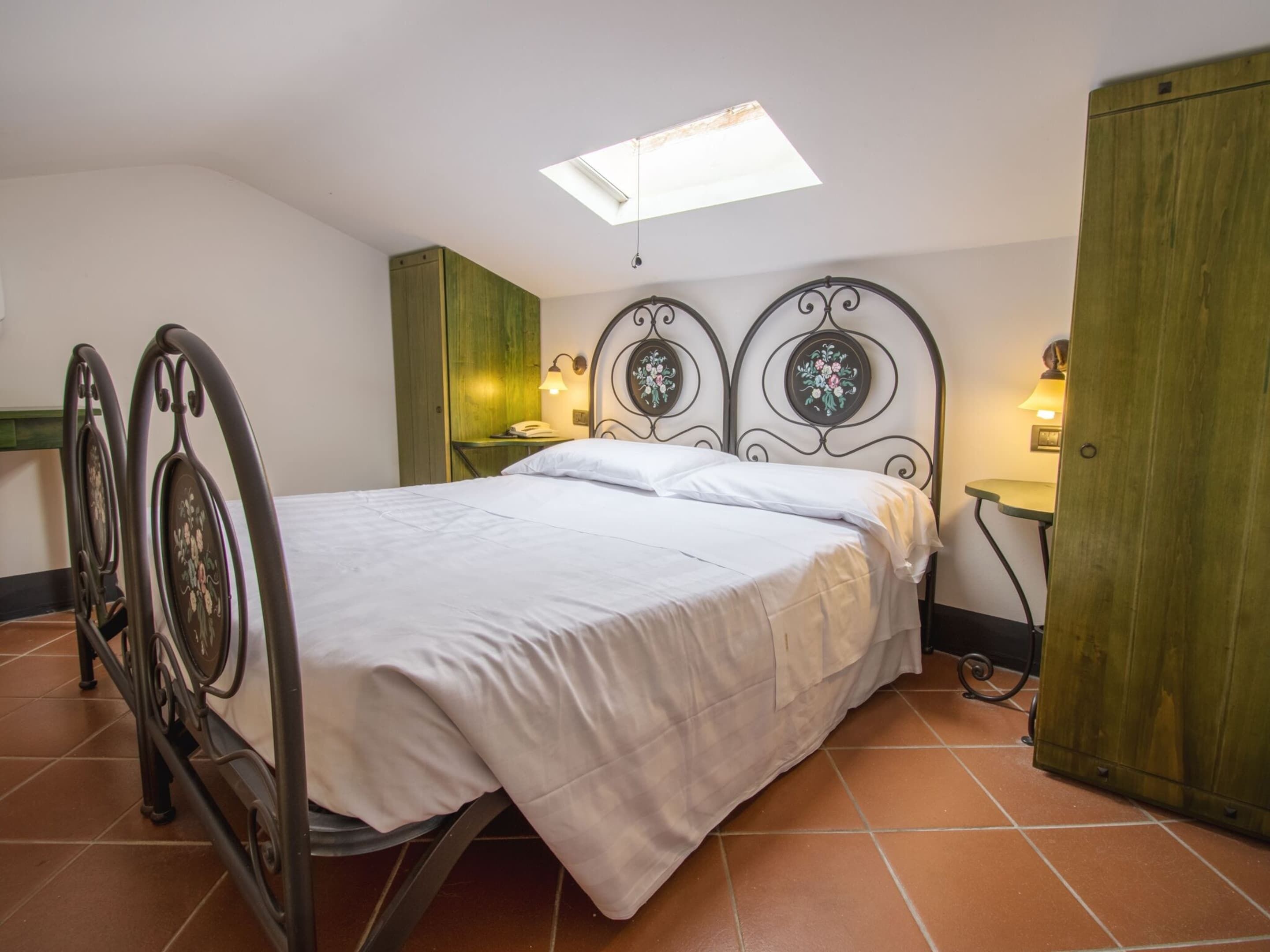A single bed with a headboard, a small bedside table, a nightstand, a wardrobe, and a skylight.
