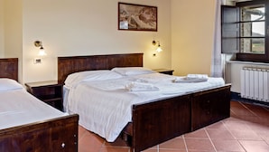 Ein Schlafzimmer mit einem hölzernen Bett, zwei Nachttischen, einem Schreibtischchen, einem Fenster mit Vorhängen und einer Heizung.