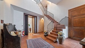 A spacious foyer with a staircase, a large wooden door, a dark armchair, and a patterned rug. - Vintage Holiday Home in Caselle in Pittari near Forest (Caselle in Pittari)