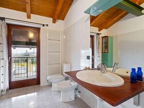 A bathroom with a wooden ceiling, a large sink, two toilets, and a view through a glass door to an outdoor balcony. - Belvilla by OYO Secluded Apartment With Balcony (Romagnano Sesia)