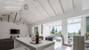 A modern living room with a central island, a flat-screen TV, and a dining area with outdoor seating. - Villa in Debeljak With Pool Near the Sea (Sukosan)