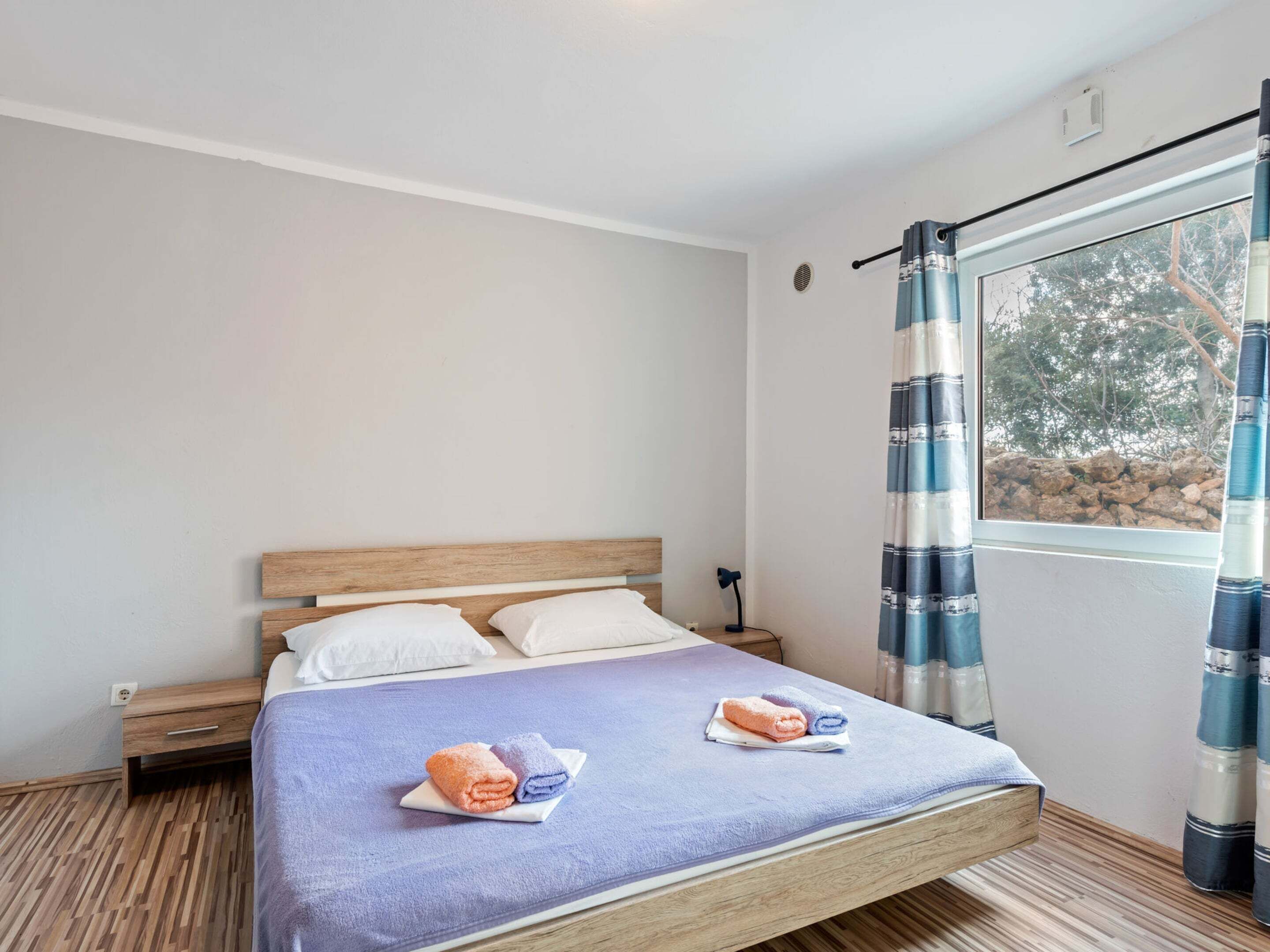 A single bed with a wooden headboard, a small bedside table, and a window with curtains.