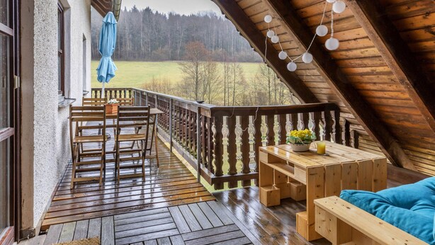Eine Holzterrasse mit Holztisch und -stühlen, einem blauen Sofa und Blick auf ein grünes Feld.