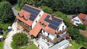 Ein zweistöckiges Haus mit Solaranlage auf dem Dach, umgeben von viel Grün.