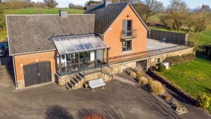 A two-story building with a glass conservatory, a brick exterior, and a balcony with outdoor seating. - Luxurious Villa in Durbuy With Swimming Pool (Durbuy)