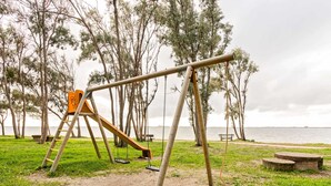 A park with a swing set, benches, and a lake in the background. - Homes in the Lagoons of Santa Giusta (Santa Giusta)