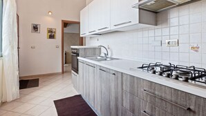 A modern kitchen with white cabinets, a gas stove, and a stainless steel sink. - Homes in the Lagoons of Santa Giusta (Santa Giusta)