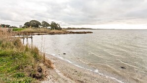 A coastal landscape with a sandy beach, a wooden pier, and a distant tree line. - Homes in the Lagoons of Santa Giusta (Santa Giusta)