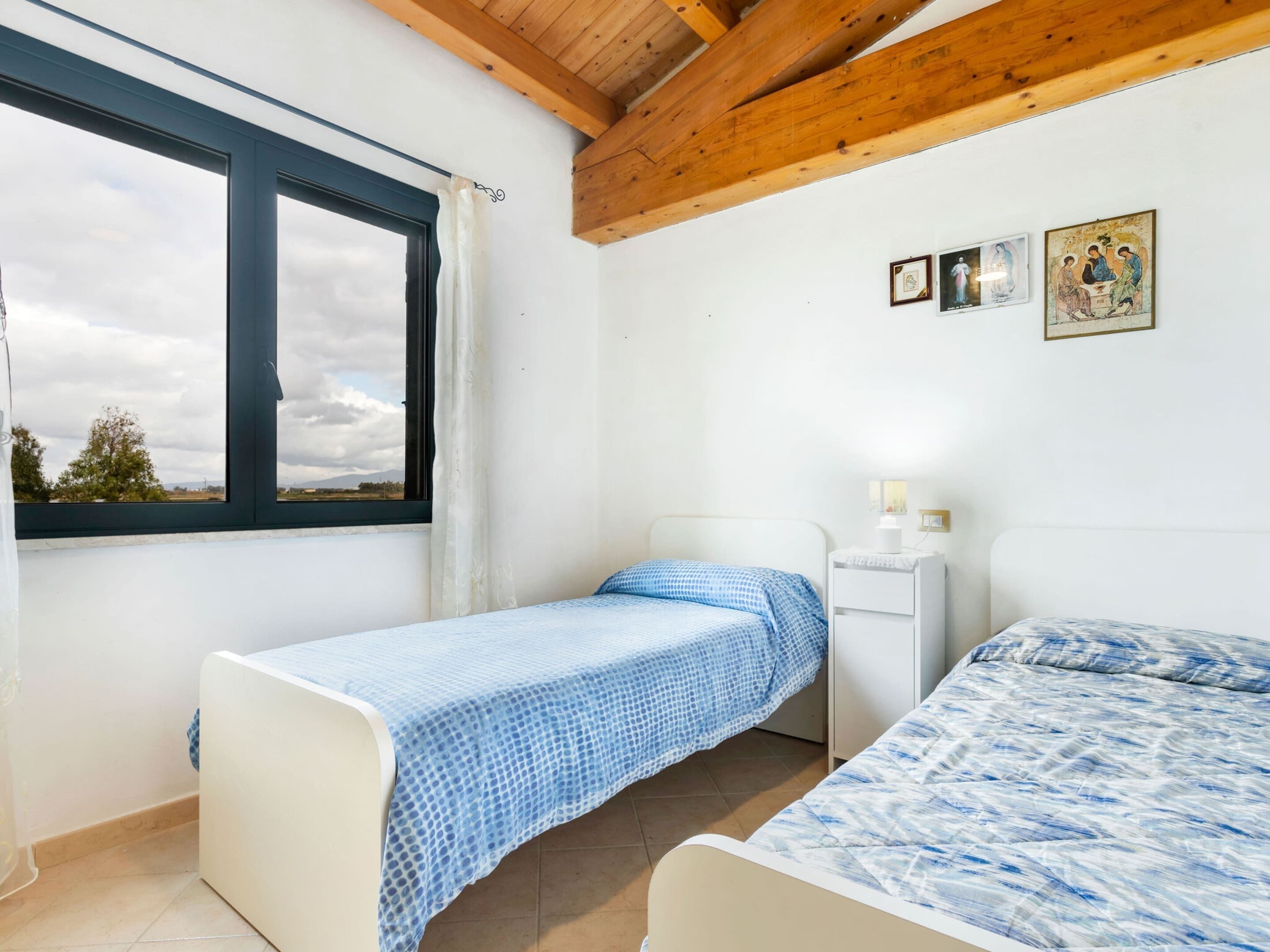 Een slaapkamer met twee bedden, een raam met gordijnen, een nachtkastje met een lamp en een kunstwerk aan de muur.
