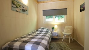 A small bedroom with a bed, a chair, a lamp, and a window. - Holiday Home in Meijel Near De Groot Peel Park (Meijel)