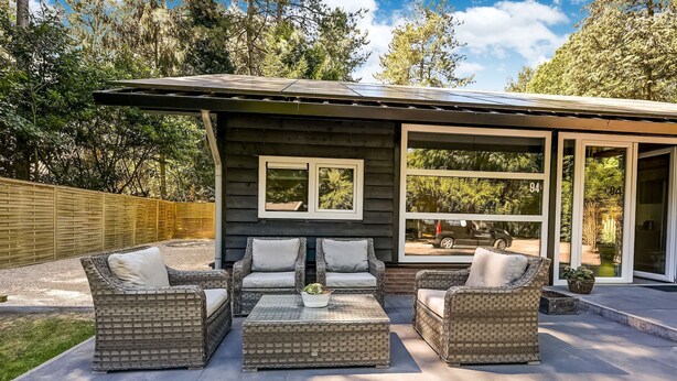 A patio area with wicker furniture and a small table, surrounded by a wooden fence and trees. - Holiday Home in Meijel Near De Groot Peel Park (Meijel)