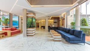 A spacious lobby with a long blue sofa, a red sofa, and a wooden bench area. - Apart Hotel Tarsis Club (Sunny Beach)