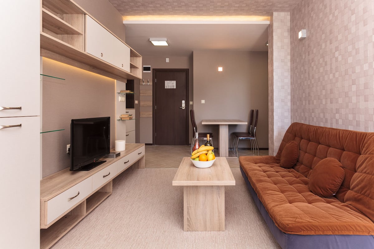 Una sala de estar moderna con un televisor de pantalla plana, una mesa de centro de madera con fruta y un sofá marrón.