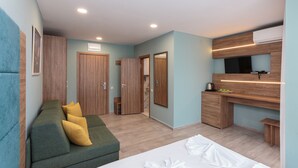 A modern bedroom with a green sofa, a bed with white linens, a built-in TV, and a wooden wardrobe. - Apart Hotel Tarsis Club (Sunny Beach)