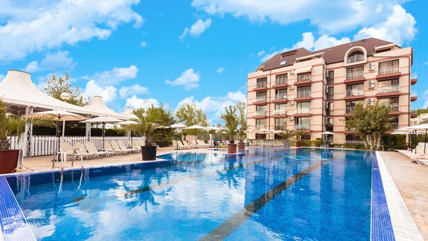 A swimming pool with lounge chairs and umbrellas, surrounded by a multi-story building with balconies. - Apart Hotel Tarsis Club (Sunny Beach)