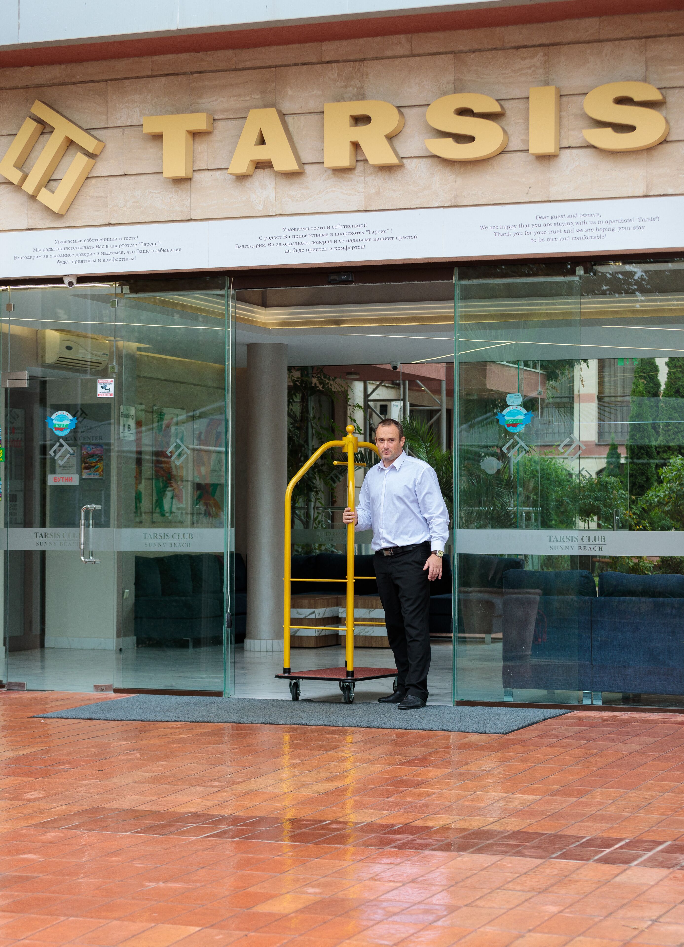 A man standing in front of a TARSIS hotel entrance with a luggage cart.