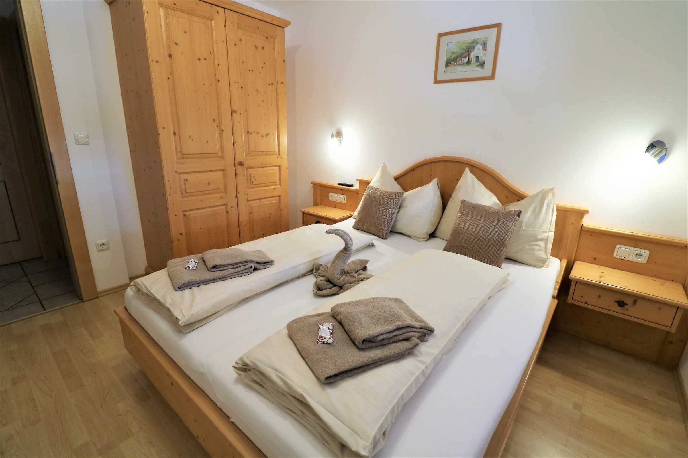 Un lit double avec une tête de lit en bois, deux tables de chevet, une armoire en bois et un luminaire fixé au mur.