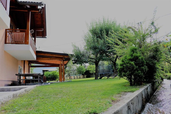 A residential building with a balcony, a wooden pergola, and a grassy yard.