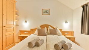 A double bed with two pillows, a wooden nightstand, a wooden wardrobe, and a framed picture on the wall.