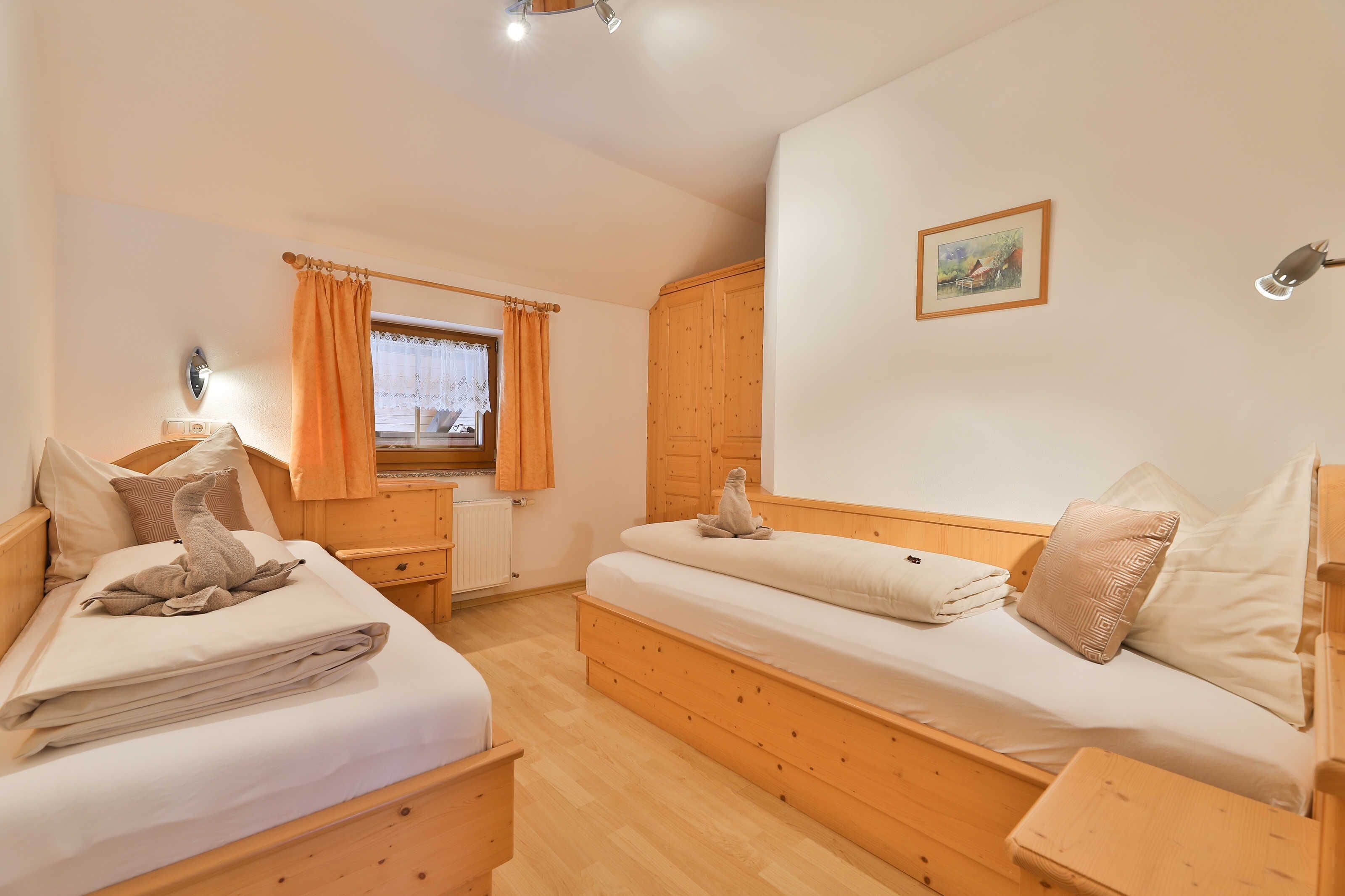 A bedroom with two wooden beds, a window with curtains, a radiator, a wooden wardrobe, and a framed picture on the wall.