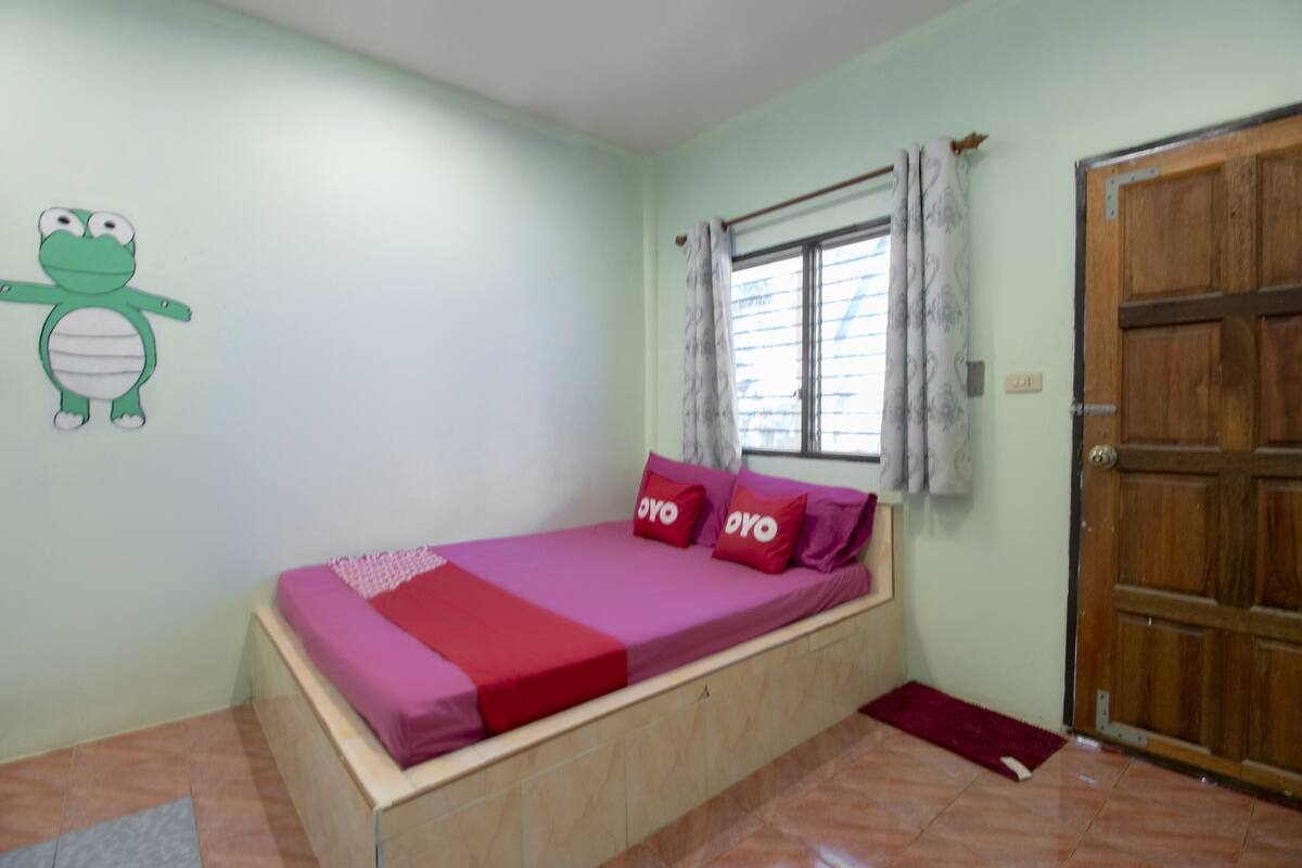 A room with a bed, a window with curtains, a wooden door, and a wall decoration.