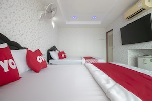 A hotel room with two beds, a TV, an air conditioner, and a fan.