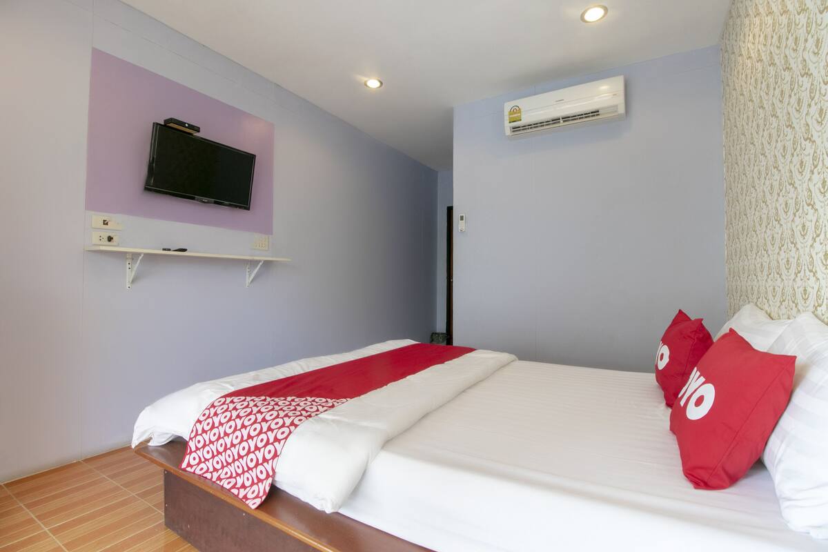 A hotel room with a bed, a mounted TV, an air conditioning unit, and a patterned curtain.