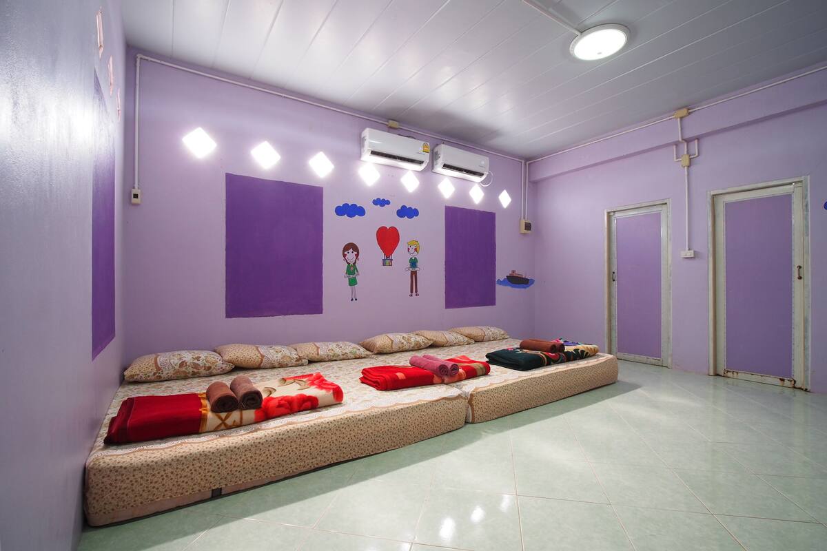 A room with a long bed, air conditioning units, and a wall with cartoon characters.