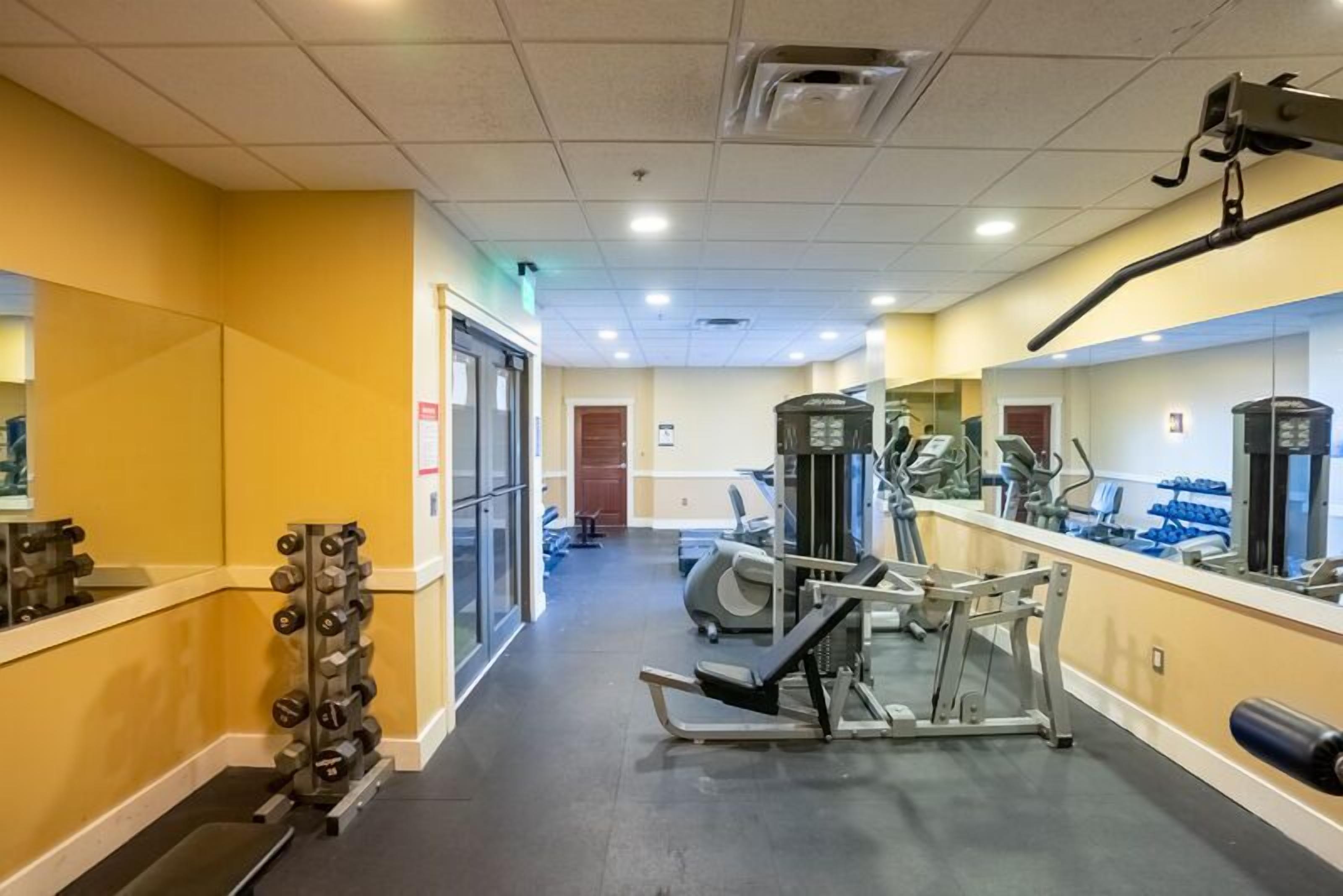 A gym with exercise equipment, mirrors, and a weight rack.