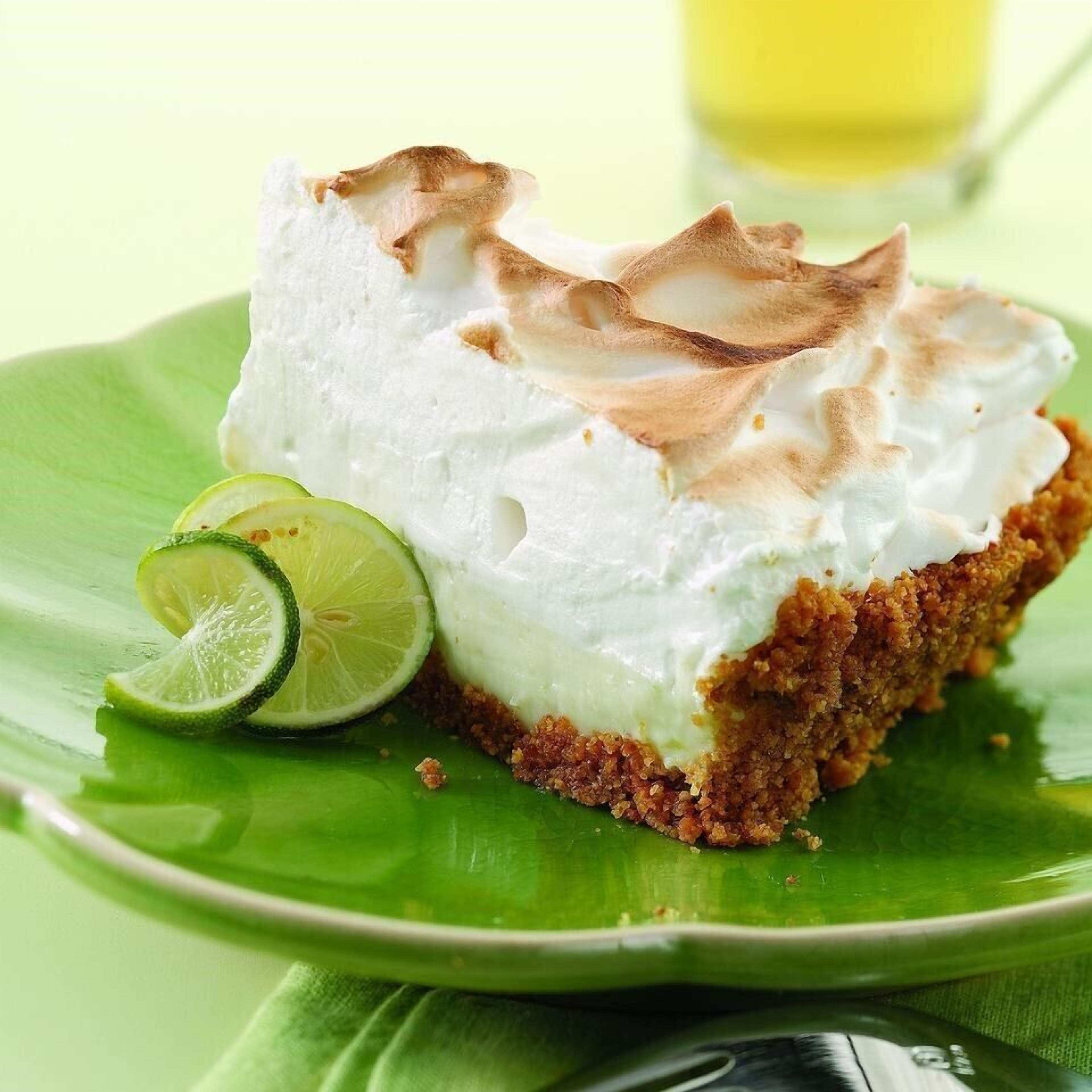 A slice of cake with meringue on top, served on a green leaf plate with a slice of lime.