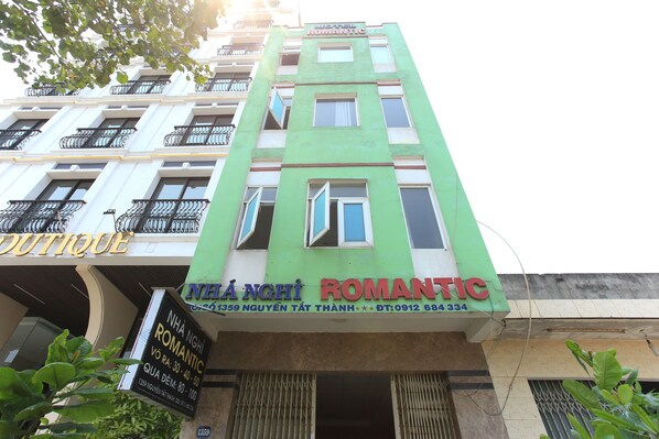 Um edifício com fachada verde e várias janelas. Há uma placa com 'NHA NGHI ROMANTIC' e outra com 'NHA NGHI'.