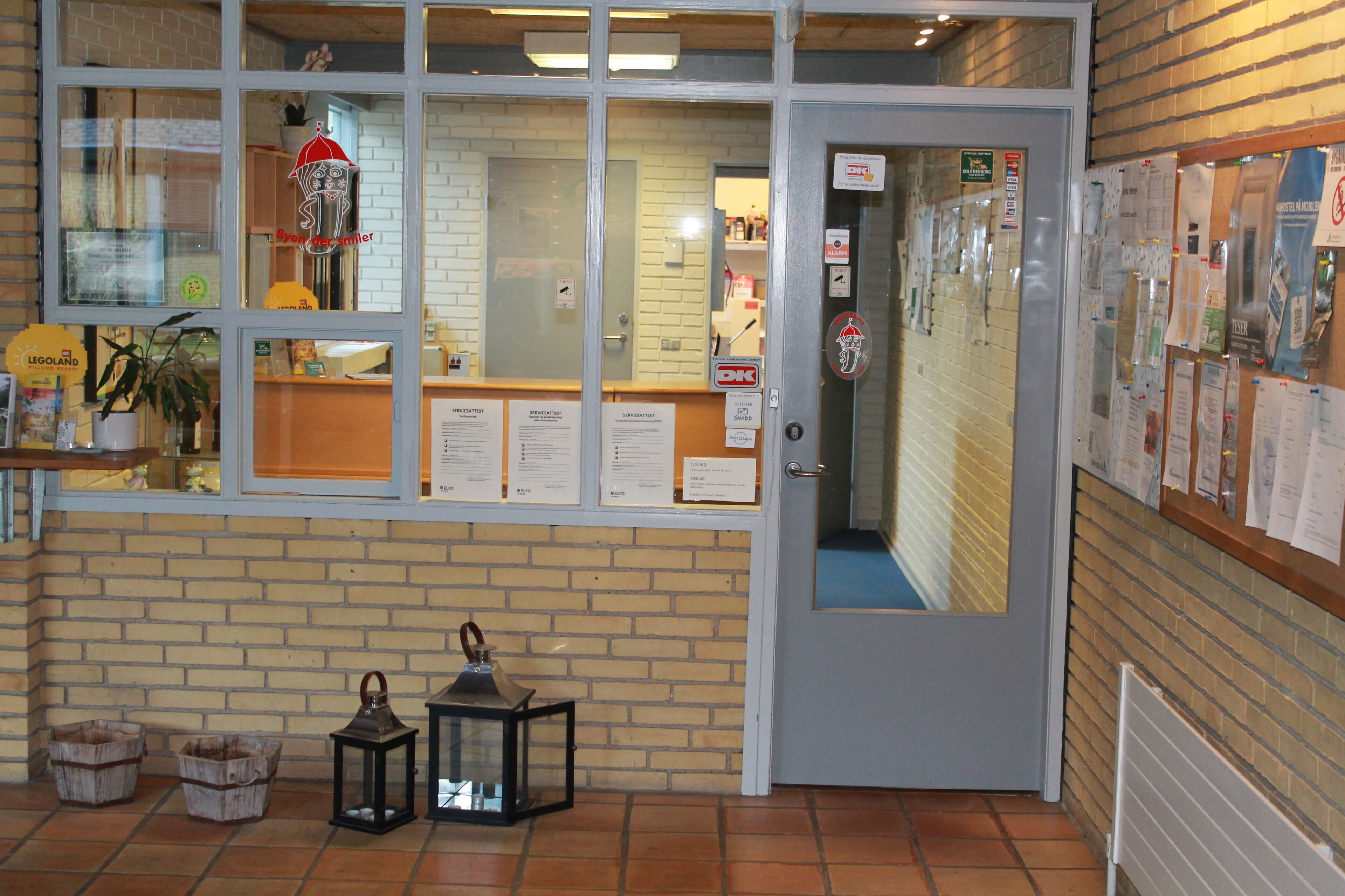 A reception area with a brick wall, a glass door, and a bulletin board with various notices.