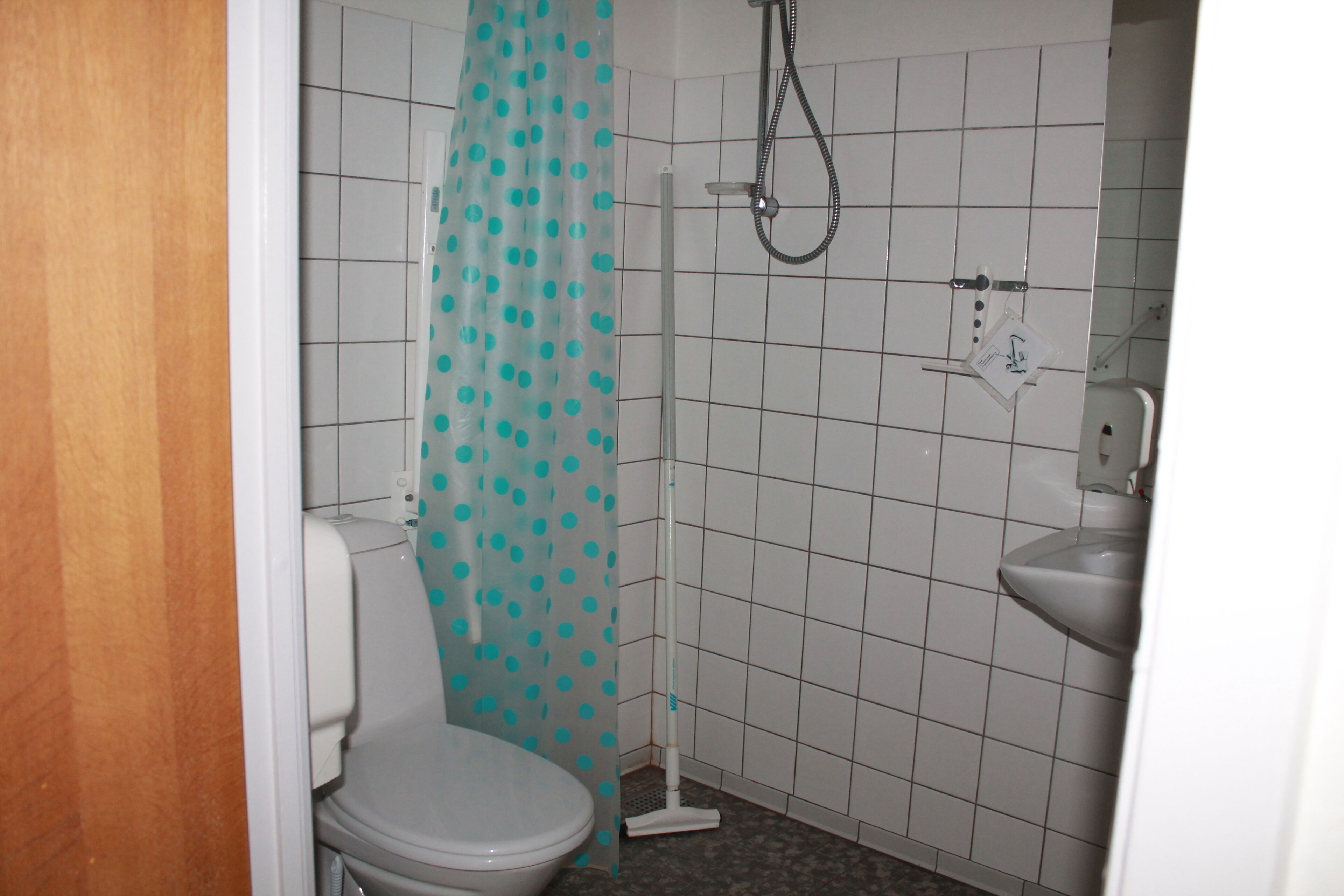 Un baño pequeño con inodoro, ducha y cortina celeste con lunares, además de un lavamanos.