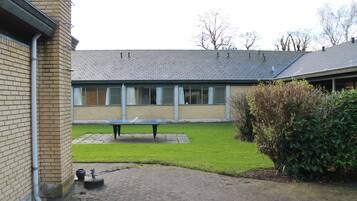 A courtyard with a brick building, a paved area, a bench, and a hedge.
