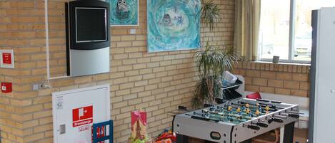 A room with a foosball table, a television, and two paintings on the wall.