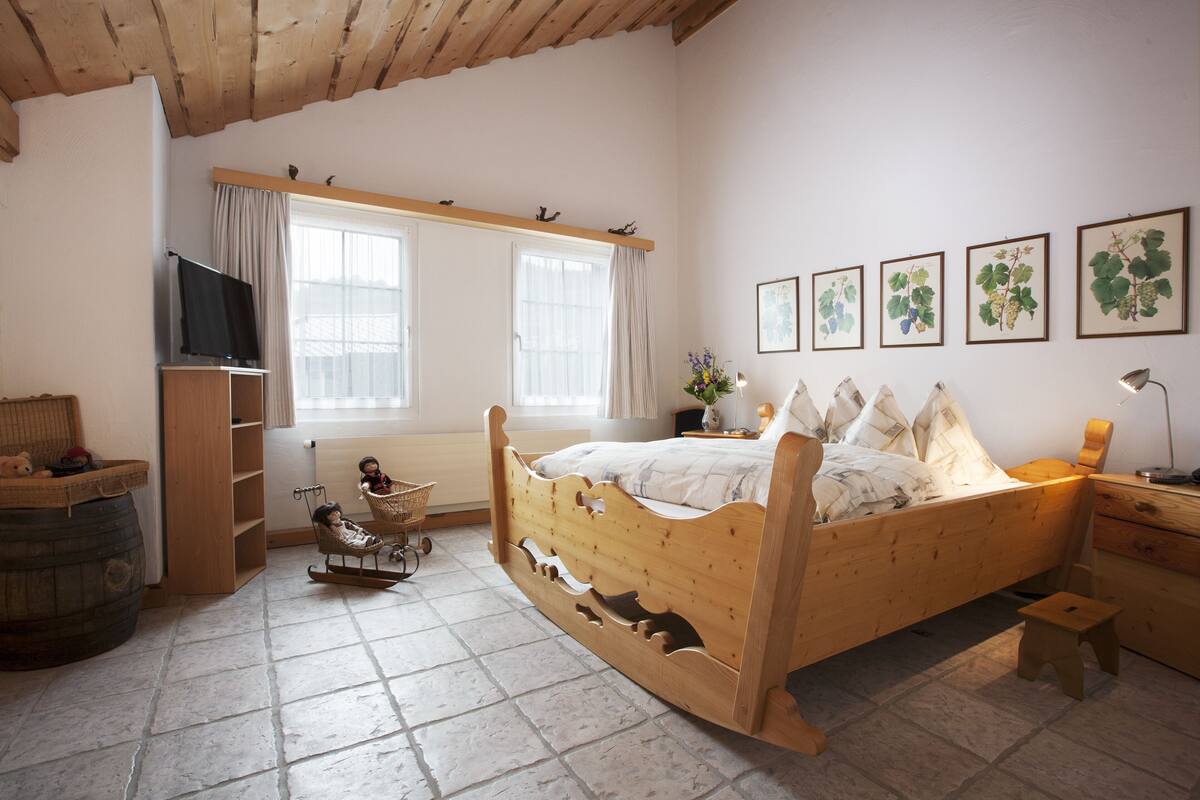 A wooden bed with a headboard, a television, a rocking chair, and a small stool.