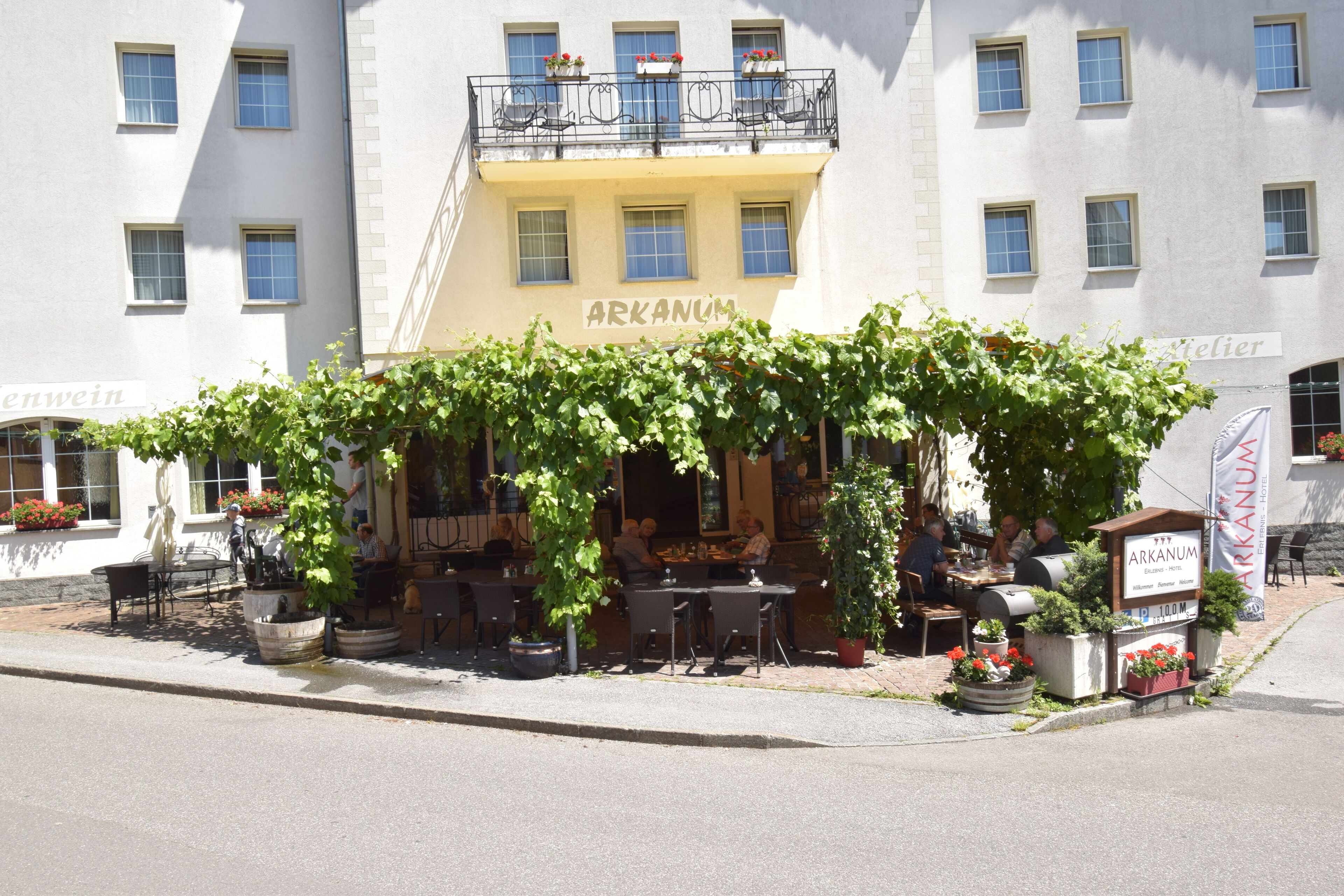 Un restaurant doté d’une terrasse, ombragée par des plantes grimpantes, et sur laquelle on peut lire l’inscription « ARKANUM ».