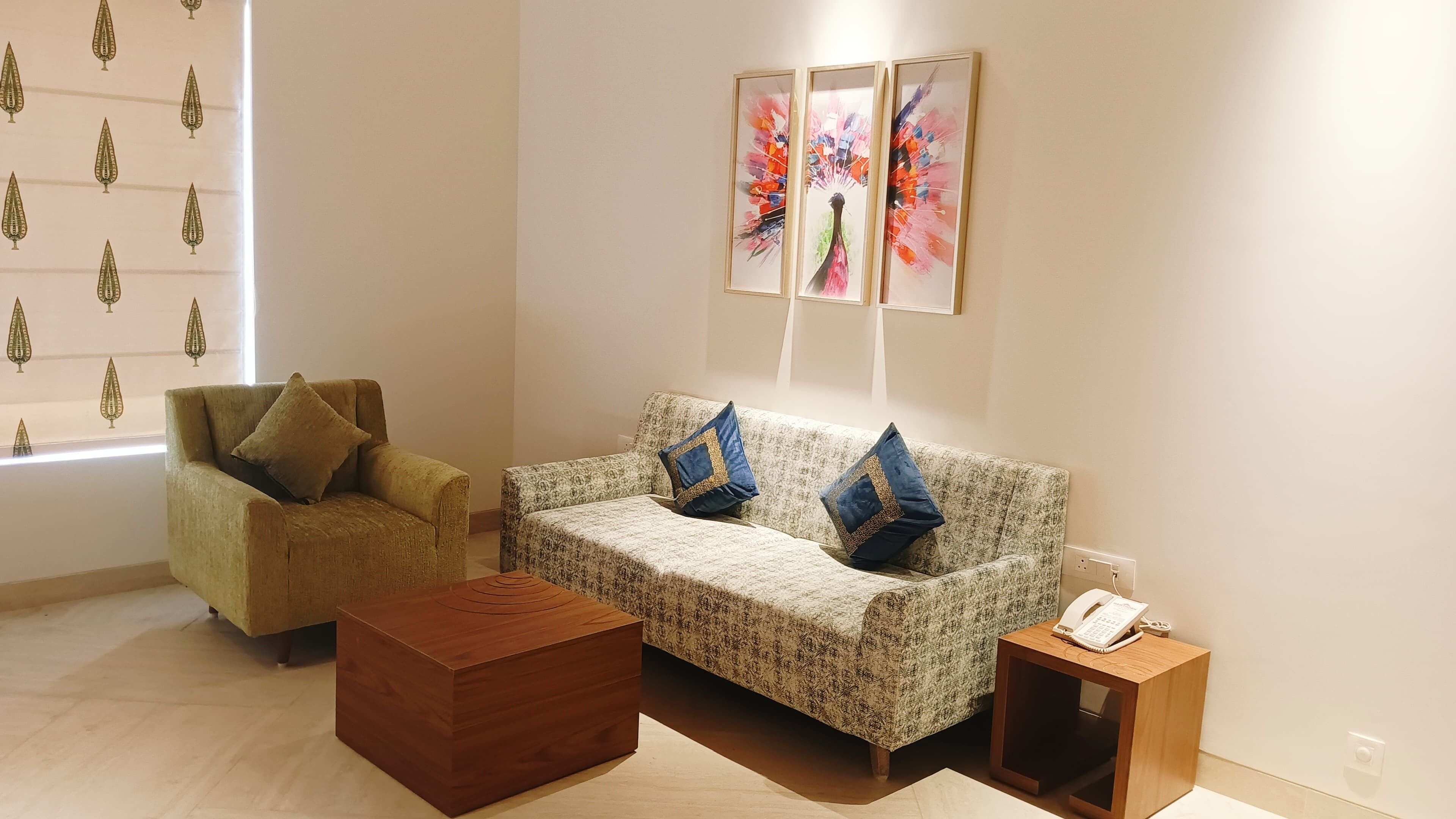 A living room with a sofa, armchair, ottoman, and a small wooden side table with a phone.