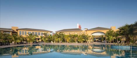 A hotel pool area with a clear blue pool, palm trees, and a building with a flag.