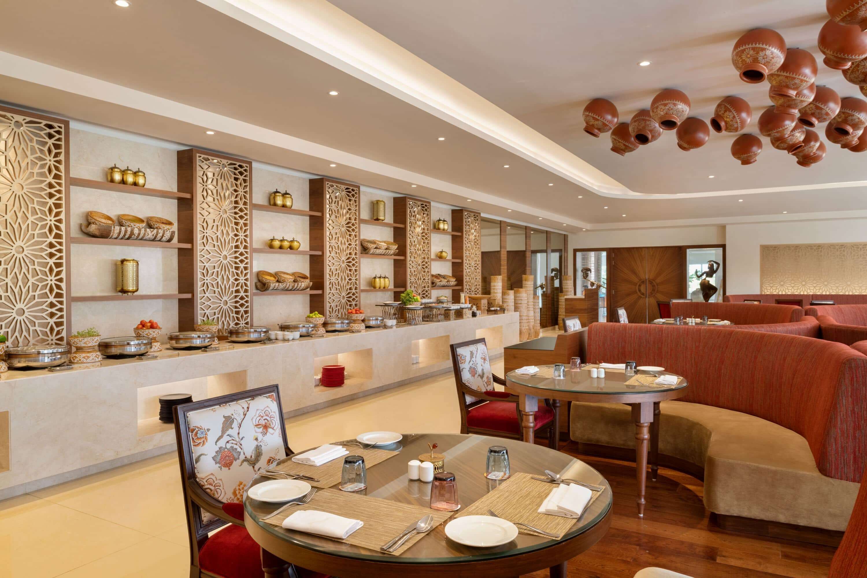 A restaurant with round tables, red upholstered seating, decorative wall panels, and a variety of dishes on shelves.