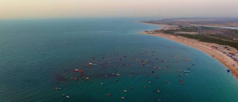 An aerial view of a coastal area with a beach, boats, and a distant cityscape.